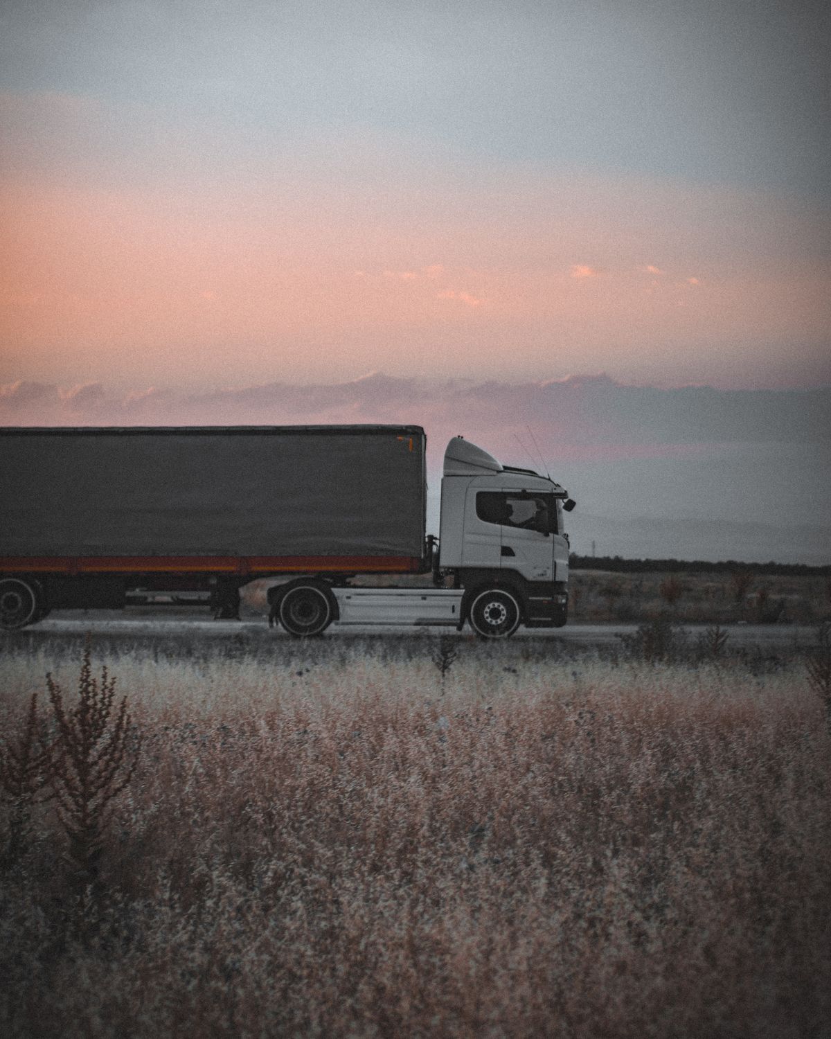 A semi-truck parked roadside under a soft sunrise sky